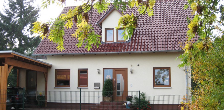 Einfamilienhaus mit Gaube, hellem Putz und Holzcarport vor dem Eingangsbereich